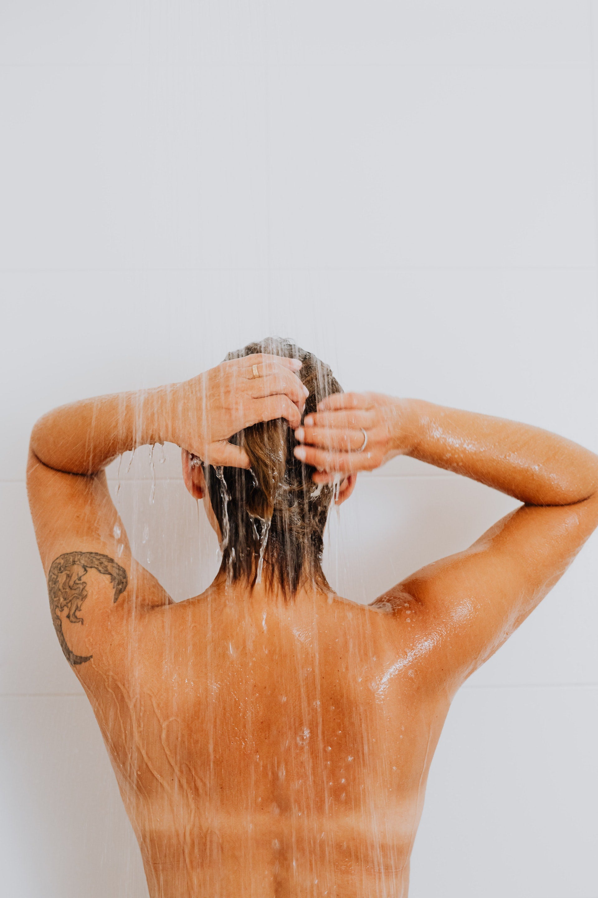 person washing hair in shower with back turned 